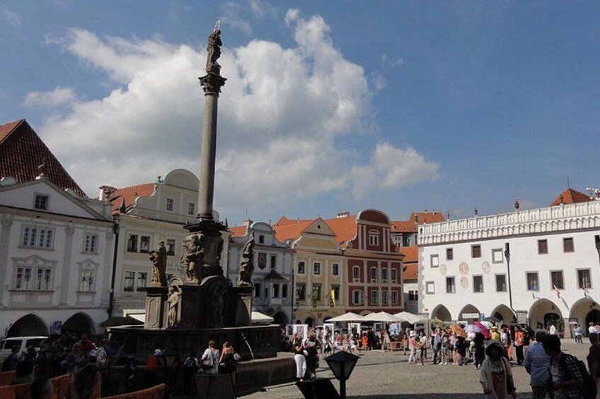 A public square with a central monument, historic buildings, and a crowd of people. 3
