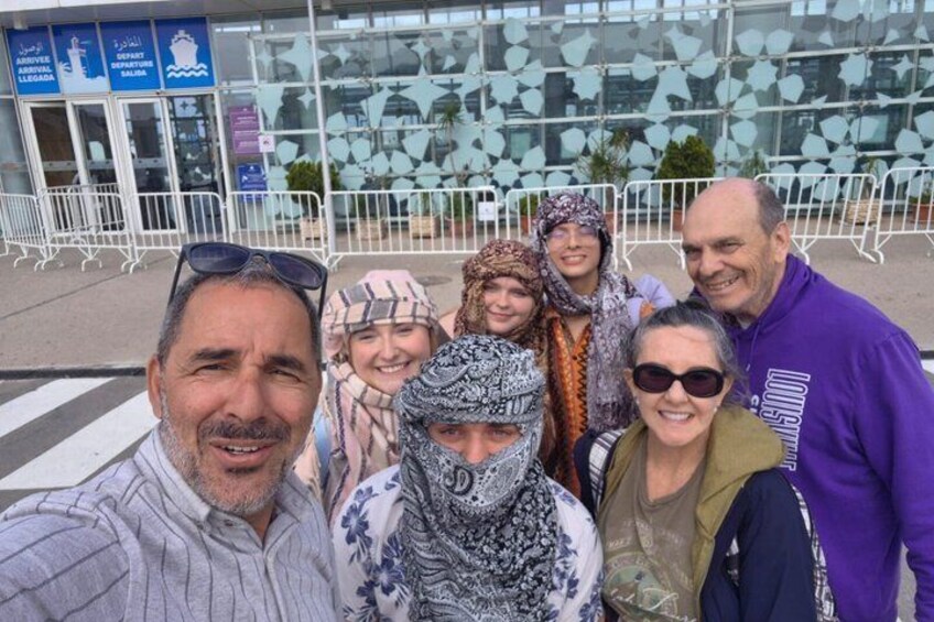 En gruppe mennesker tager en selfie foran en moderne bygning med glaspaneler og metalgelændere. 1