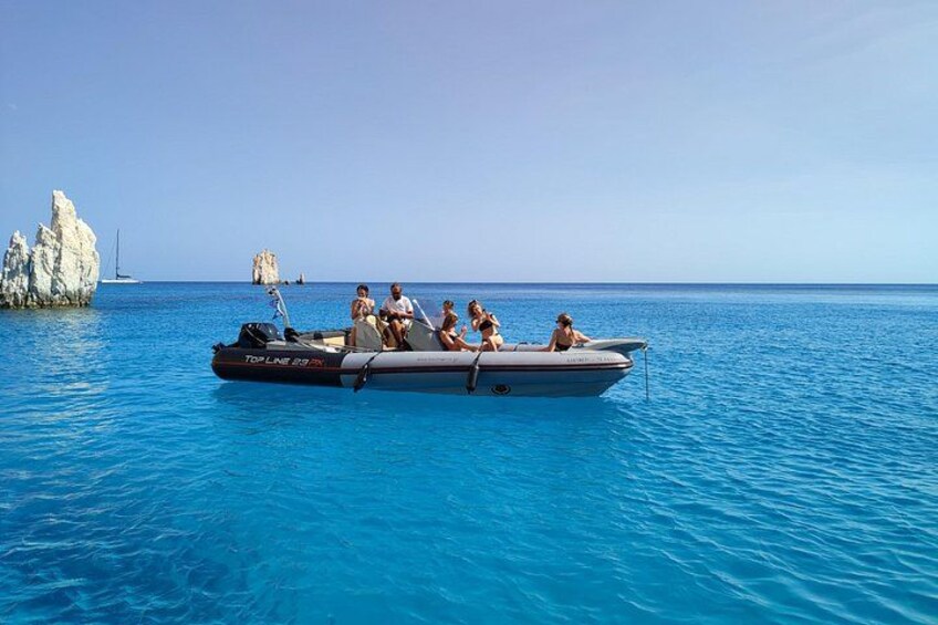 Een boot met mensen op een heldere blauwe zee, rotsachtige kliffen en een zeilboot in de verte. 4