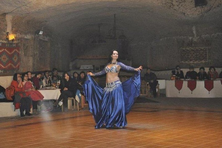 Una donna danza con un abito blu in una stanza poco illuminata, mentre un pubblico è seduto a tavoli. 4
