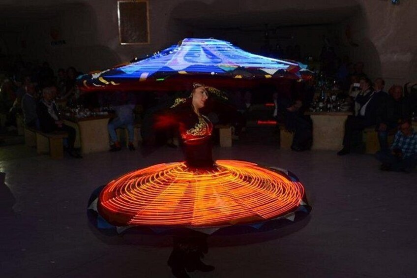 Una persona che esegue una danza in una stanza scarsamente illuminata, con un pubblico seduto tutt'intorno. 1