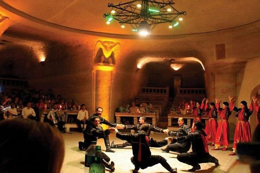 Un gruppo esegue un ballo tradizionale in un edificio storico, scarsamente illuminato, con architettura in pietra e un lampadario. 5