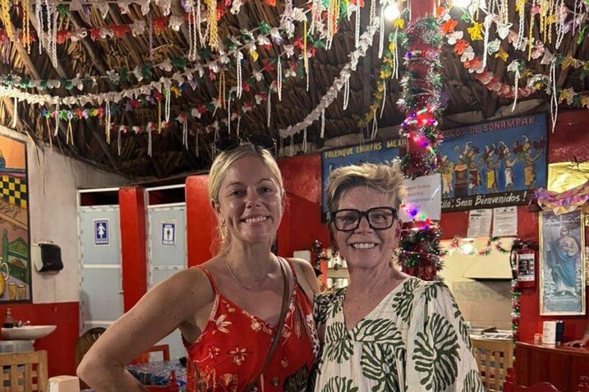 Two people in a decorated indoor space with hanging ornaments and a poster in the background. 4
