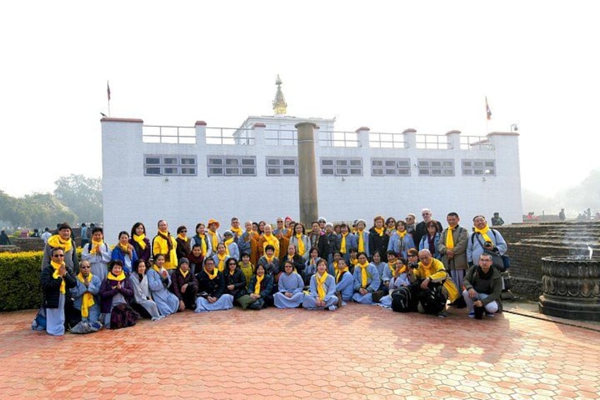 A group of people posing in front of a white building with a flag, a fountain, and a statue in the background. 2