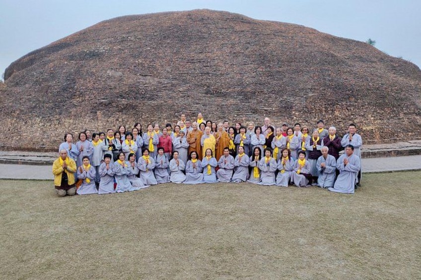 A group of people in traditional attire posing in front of a large, ancient stone structure. 4
