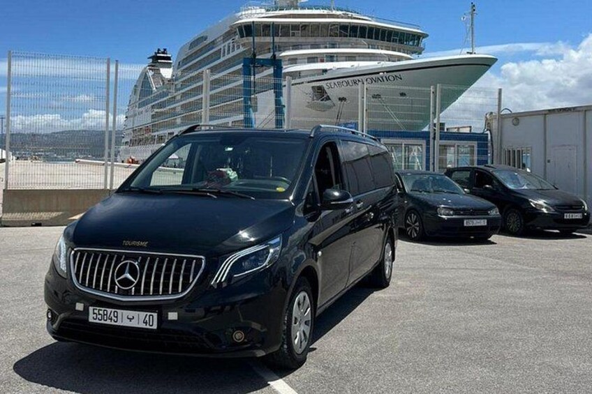 En svart Mercedes-Benz-SUV står parkerad på en parkeringsplats, med ett kryssningsfartyg och en byggnad i bakgrunden som har skylten ”Scafellburn Aviation”. 4