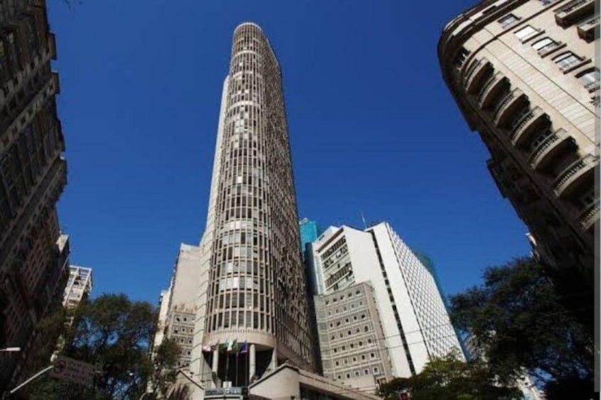 Un rascacielos alto y curvo, con fachada de entramado, rodeado de otros edificios y árboles. 5
