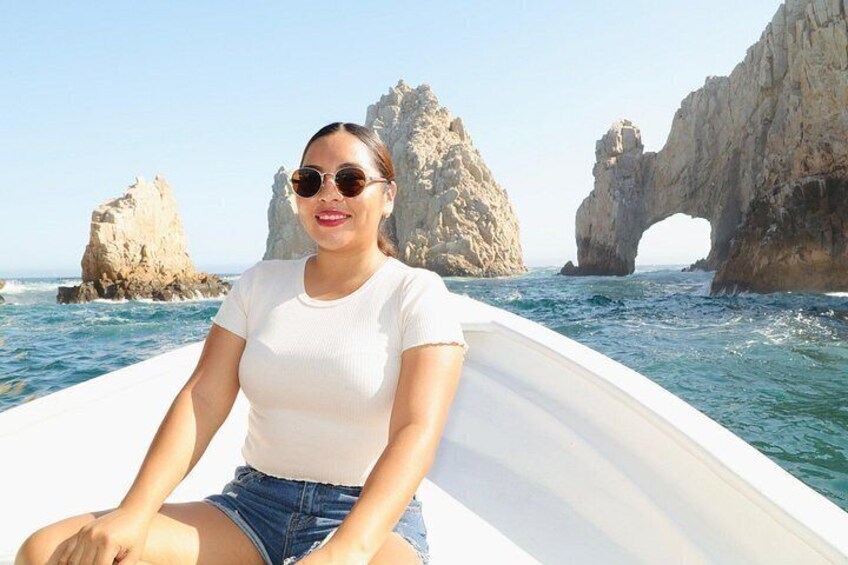 A person on a boat with a rocky coastline and arch formations in the background. 1