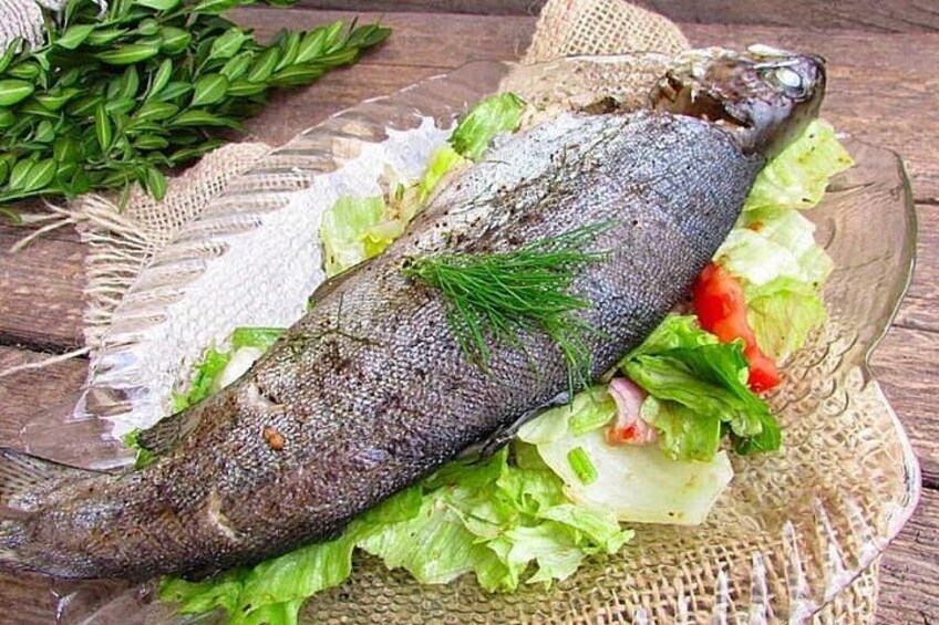 Un pescado entero en un plato con lechuga y tomates. 1