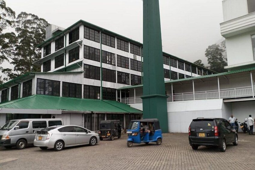A multi-story building with a green roof and white walls, surrounded by parked cars and a tuk-tuk. 4