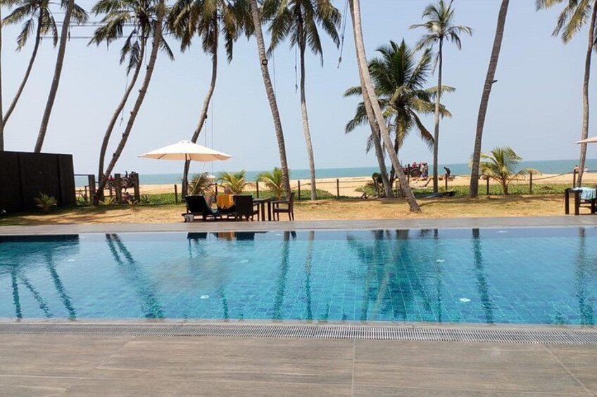 A swimming pool with lounge chairs and umbrellas, palm trees, and a beach in the background. 2