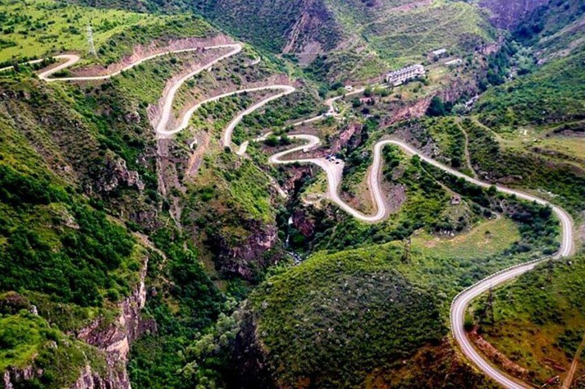 A winding mountain road through a lush valley with rocky cliffs and sparse vegetation. 5
