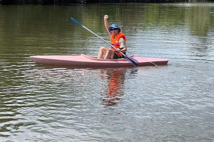 A person in a pink kayak on a calm body of water, wearing a life jacket and a helmet. 2