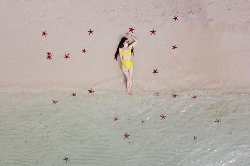 A person in a yellow swimsuit standing on a sandy surface with red star decorations. 5
