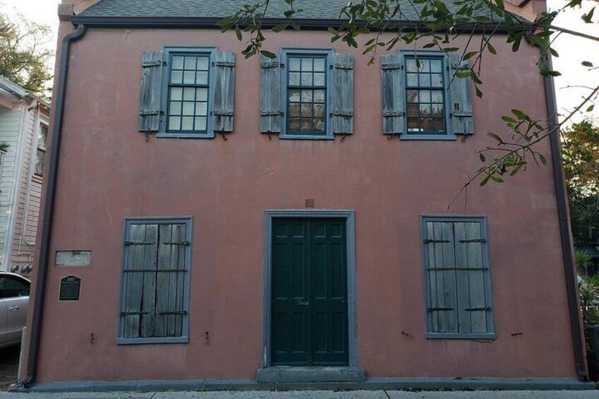 A pink building with a green door and shutters, a plaque, and a parked car. 3