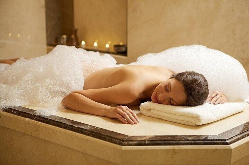 A person lying on a massage table covered with a white towel, surrounded by bubbles. 2