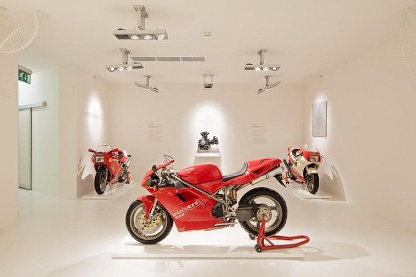 A red motorcycle on display in a white room with spotlights. 1