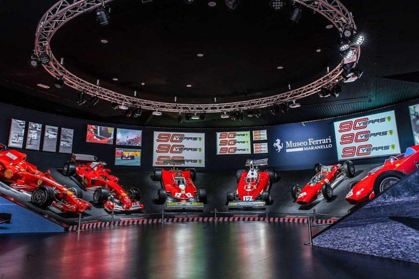 Una exhibición de museo con varios coches de carreras rojos y una plataforma de observación circular. 3