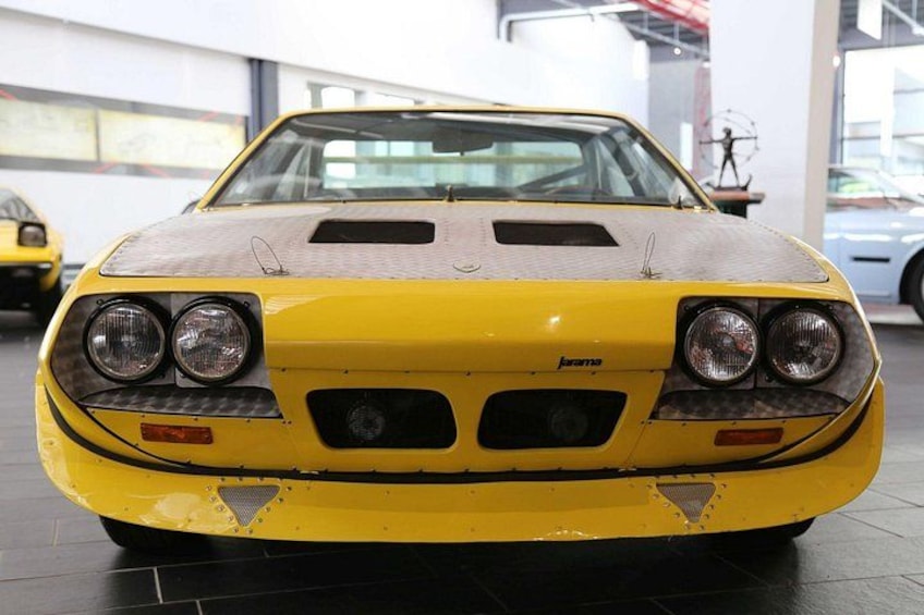 A yellow sports car with a black hood, visible headlights, and a rear spoiler. 2