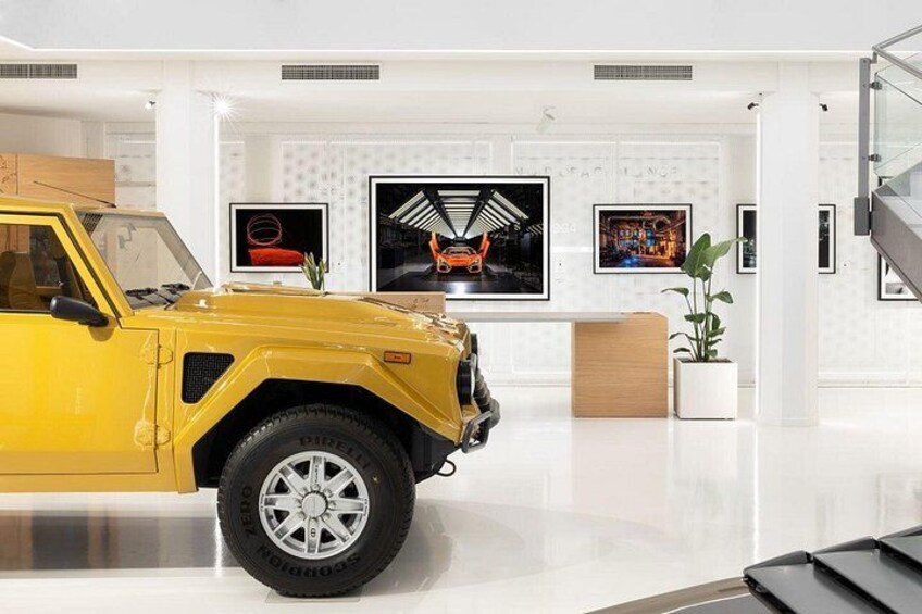 A yellow SUV in a modern, white interior space with framed artwork on the wall. 2