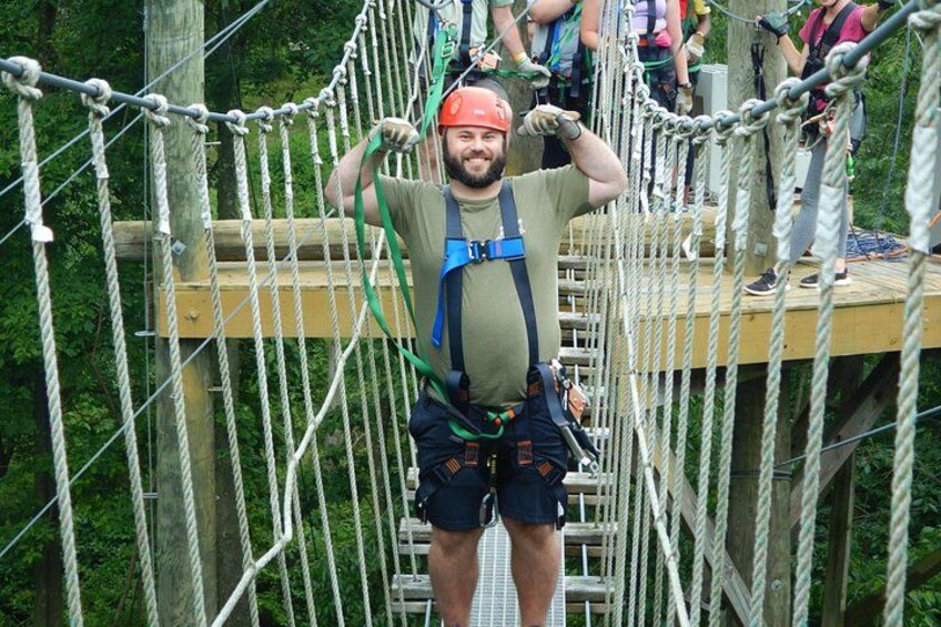 A person on a suspension bridge with safety harnesses, surrounded by greenery. 3