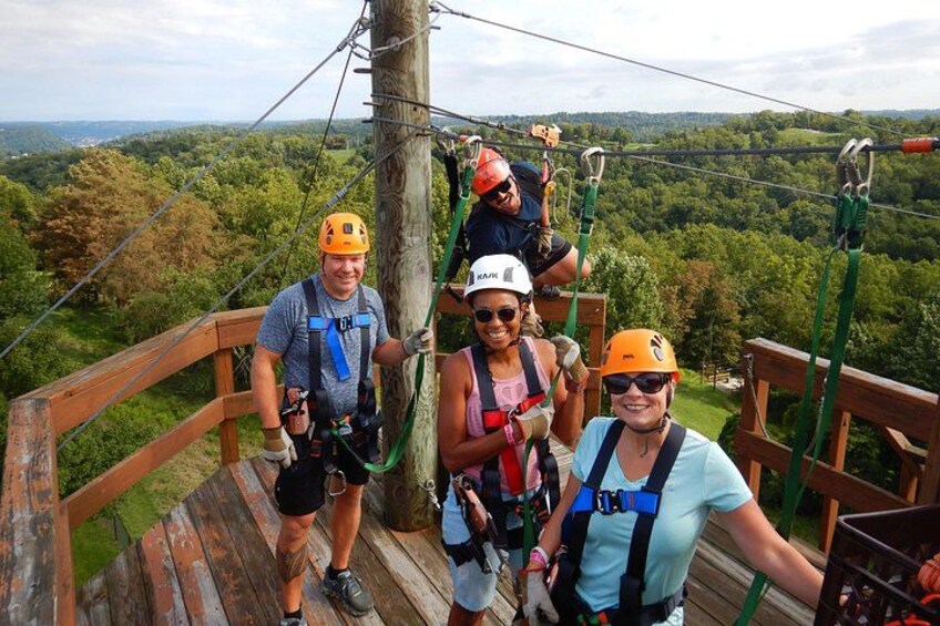 People on a wooden platform with safety harnesses, overlooking a forested landscape. 4