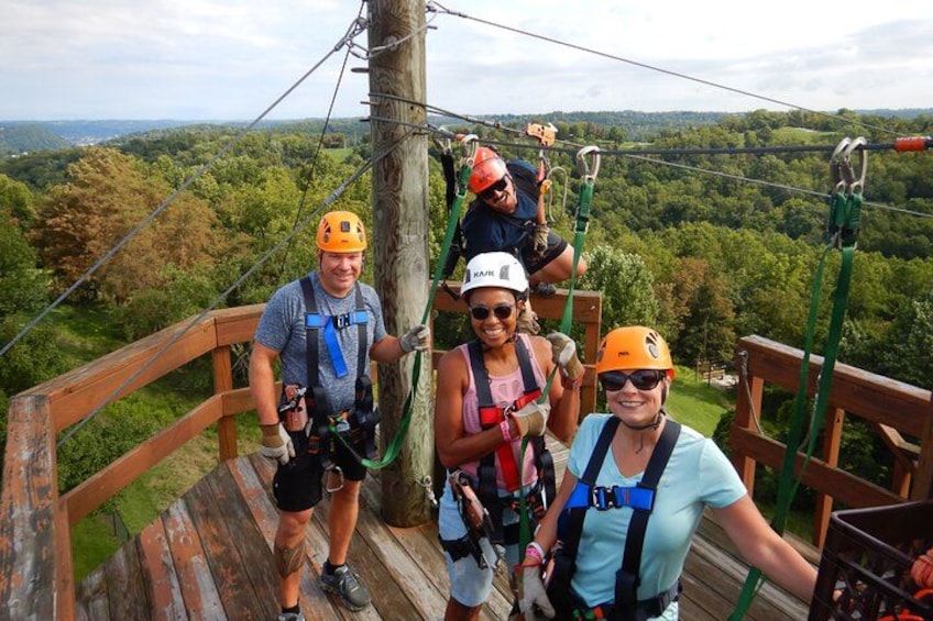 People on a wooden platform with safety harnesses, overlooking a forested landscape. 4