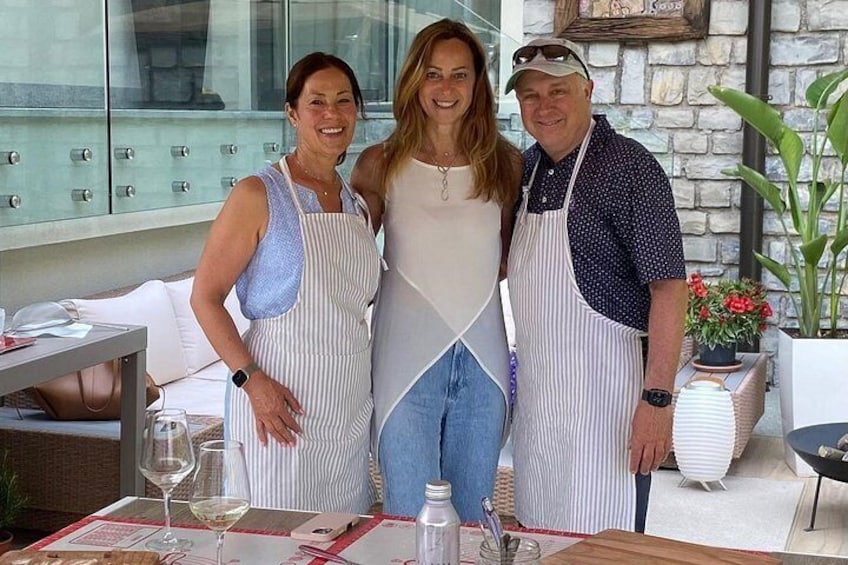 Tres personas de pie junto a una mesa, con una copa de vino, una botella de agua y un menú. 1