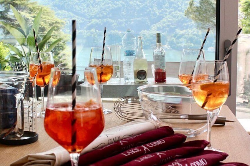 Ein Tisch mit Getränken und einer Flasche, ein Fenster mit Blick auf Bäume und Wasser, sowie eine Speisekarte mit roten Servietten. 3