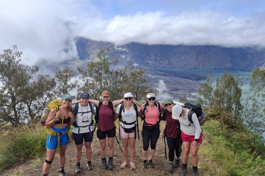 Een groep wandelaars op een bergpad, met een meer en wolken op de achtergrond. 2