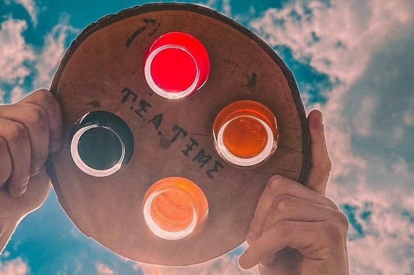 Une planche en bois avec quatre gobelets de couleurs différentes, tenus dans des mains, sur fond de ciel. 1