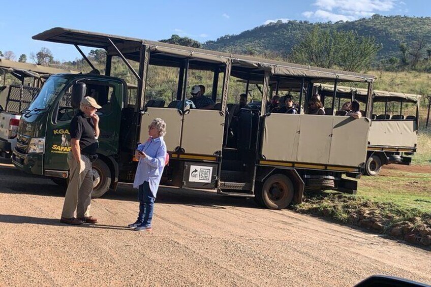 A safari vehicle with passengers and a guide standing beside it. 5