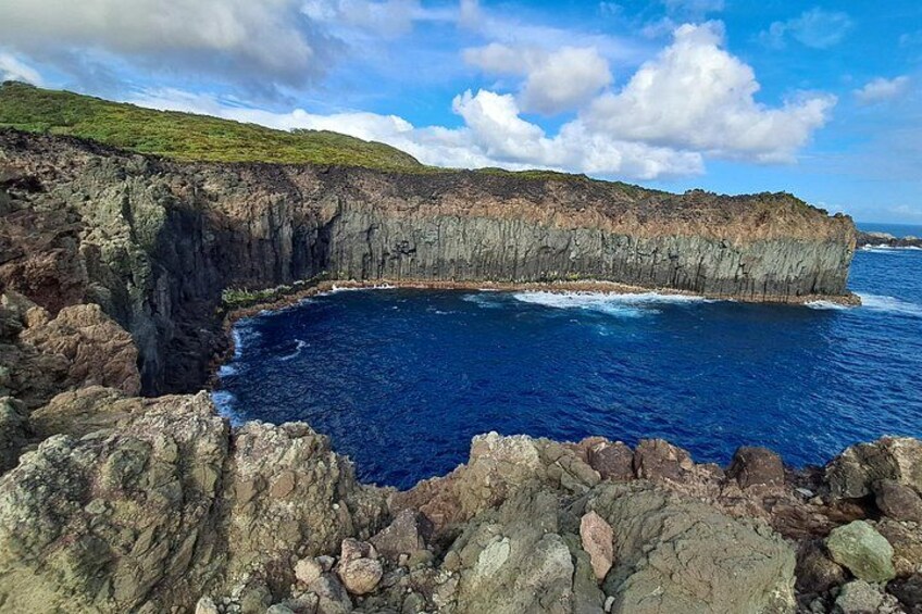 Un acantilado costero con un mar azul intenso, primer plano rocoso y cielo despejado. 2