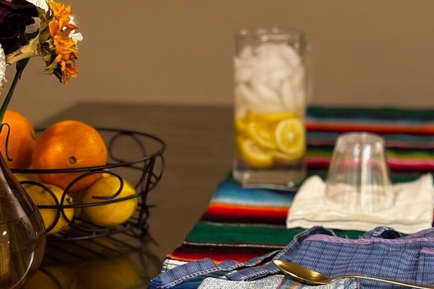 Una mesa con un jarrón de flores, un vaso de limonada, naranjas y un mantel a rayas. 2