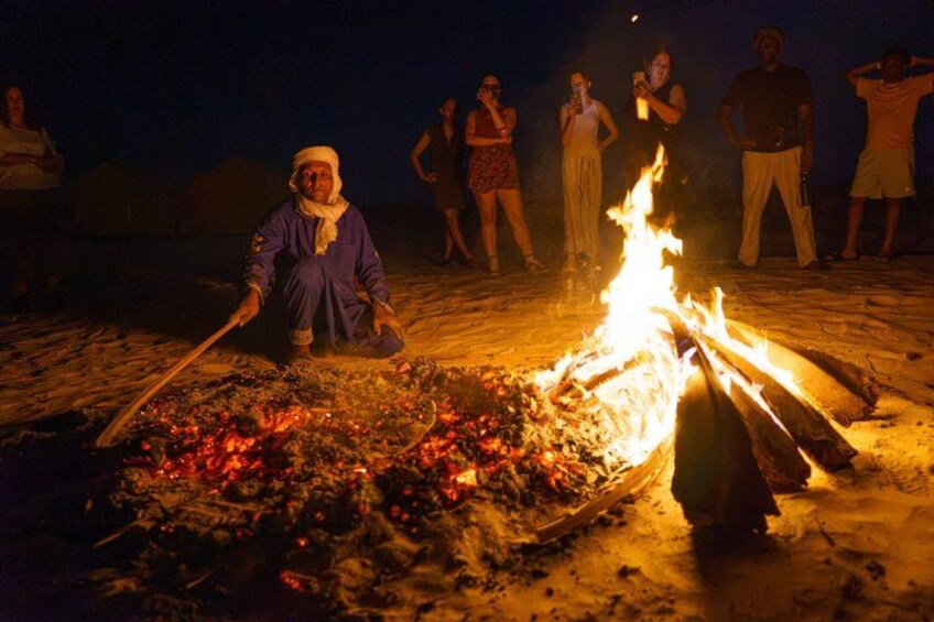 A person cooking over an open fire at night. 5