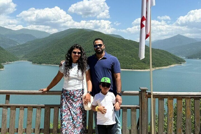 A family on a wooden deck overlooking a lake with mountains in the background. 2