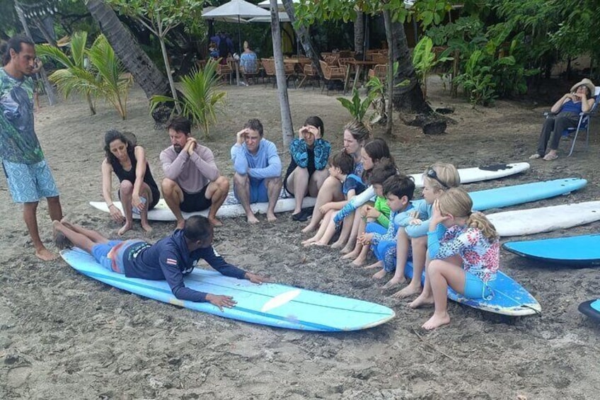 A group of people sitting on surfboards on a sandy beach, possibly learning to surf. 5
