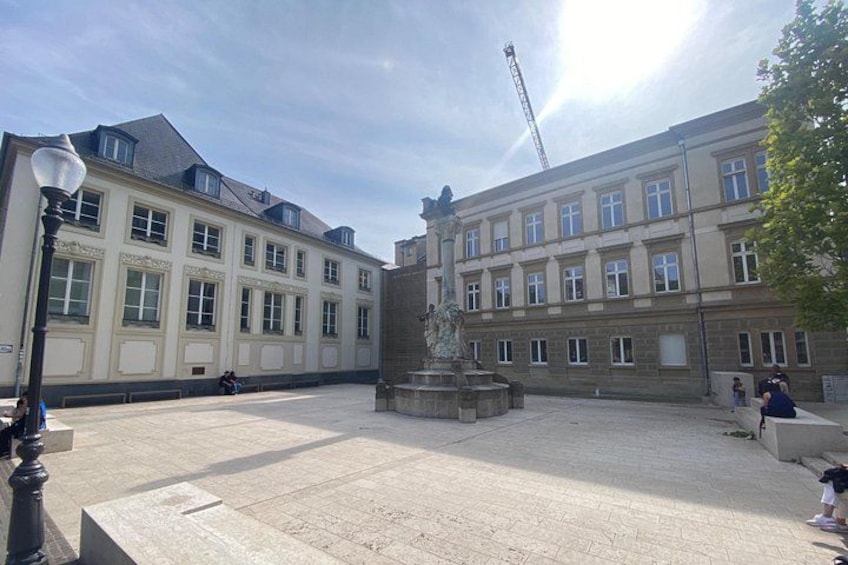 A courtyard with a fountain, buildings, and a crane in the background. 1