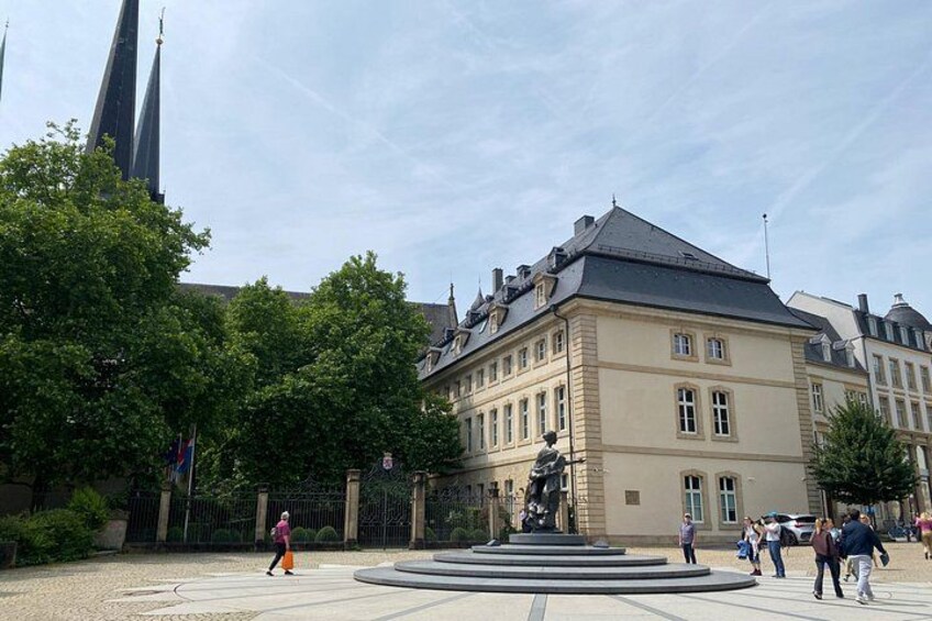 A historic building with a statue in front, surrounded by trees and a fountain. 5