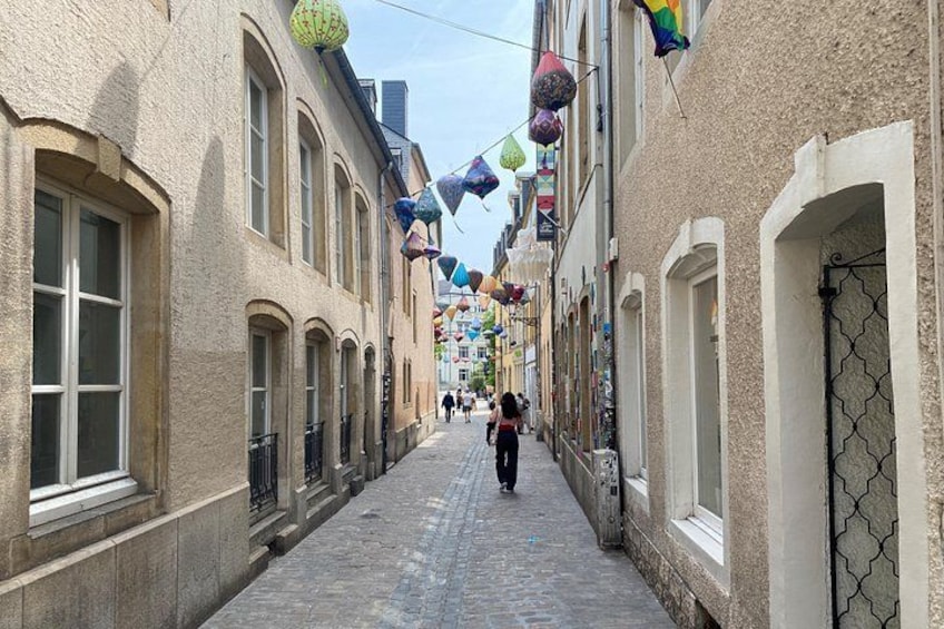 A narrow cobblestone street lined with historic buildings, decorated with colorful hanging ornaments. 4