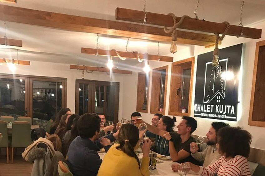 Un grupo de personas cenando en un restaurante con vigas de madera y un cartel que dice 'CHALET KUJTA'. 2
