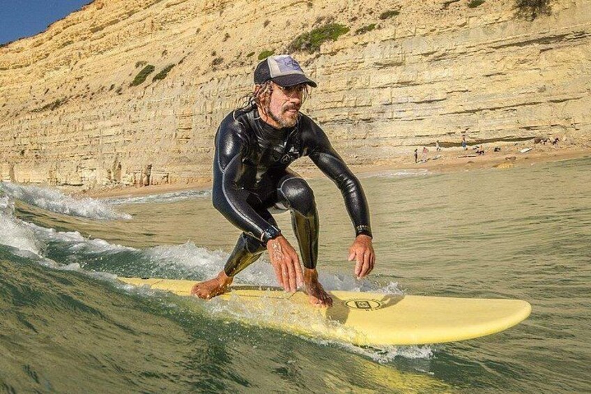 A person surfing on a yellow board in the ocean with cliffs in the background. 2