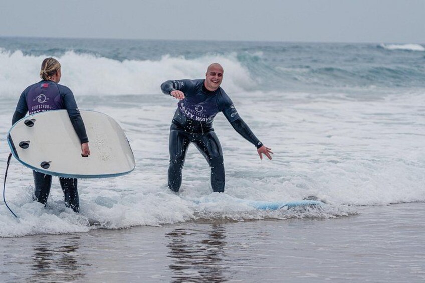 Two people in wetsuits carrying surfboards on a beach with waves. 4