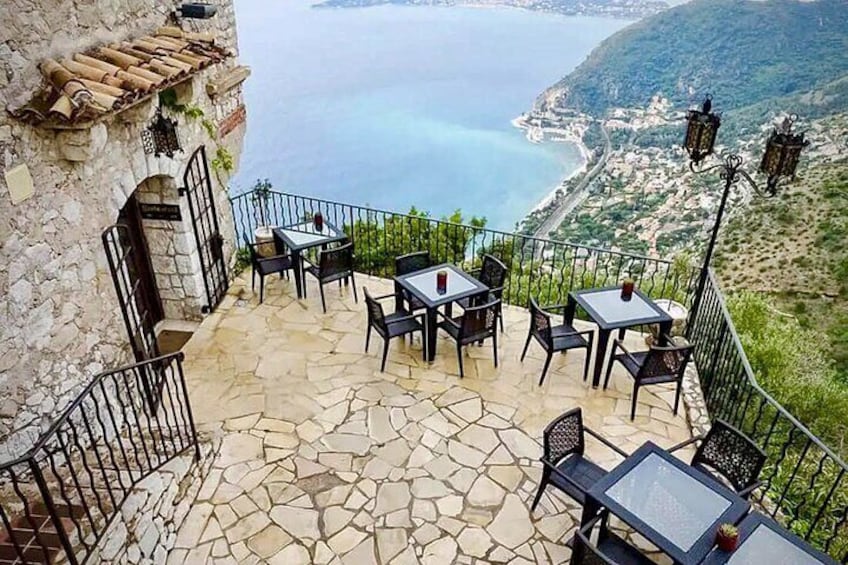 A terrace with stone flooring and tables overlooking a coastal landscape. 1