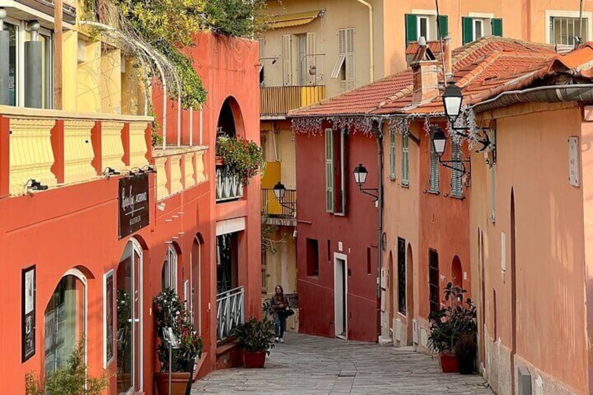 A narrow street with colorful buildings, arched doorways, and hanging plants. 2