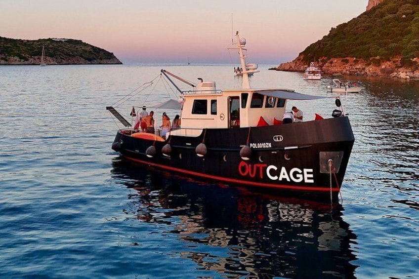 A boat named 'OUT CAGE' with people on board, docked near a rocky coastline. 1