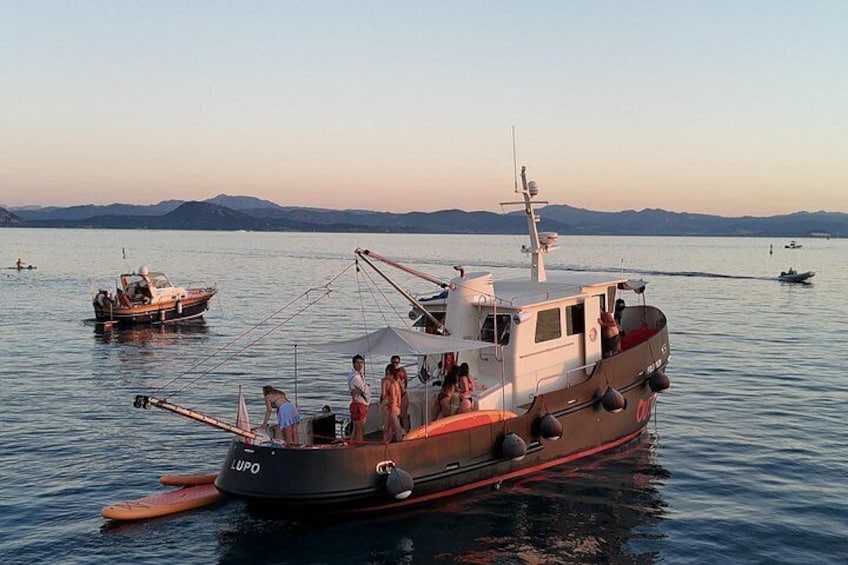 A fishing boat named 'LUPO' with people on board, docked in calm waters with other boats in the background. 4