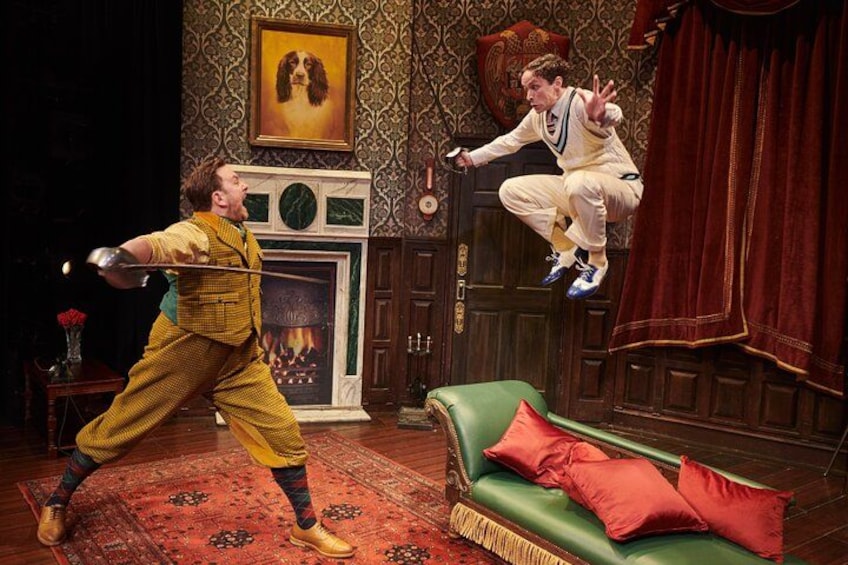 Ein inszeniertes Bild mit zwei Personen in lebendiger Pose, einem Kamin, einem grünen Sofa und einer Wand mit Muster. 5