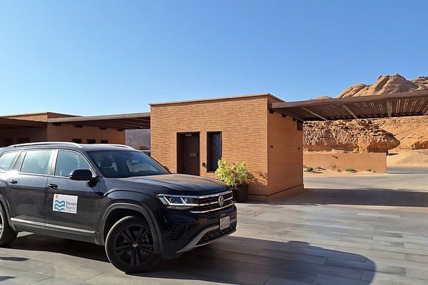 A black SUV parked in front of a modern building with a desert landscape in the background. 1