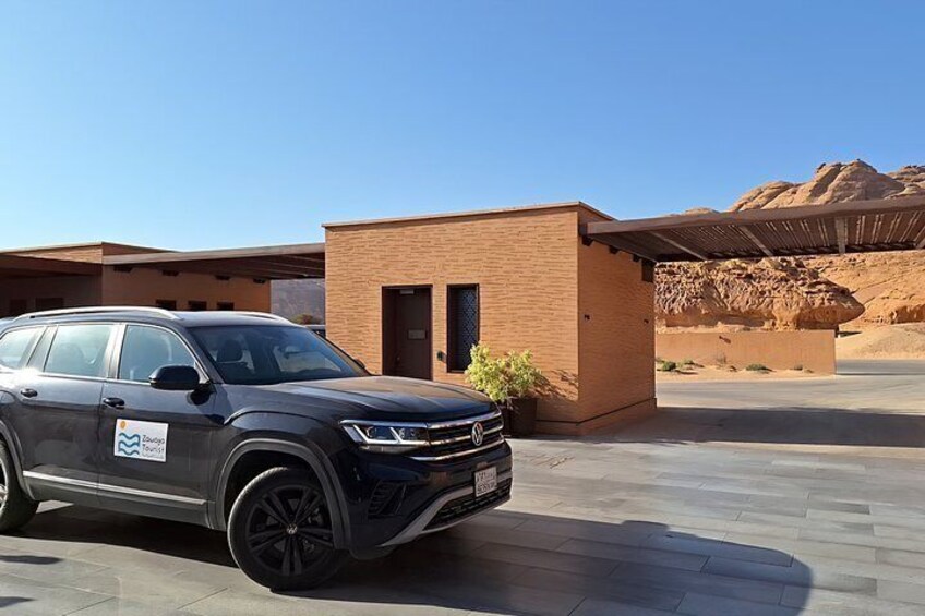 A black SUV parked in front of a modern building with a desert landscape in the background. 1
